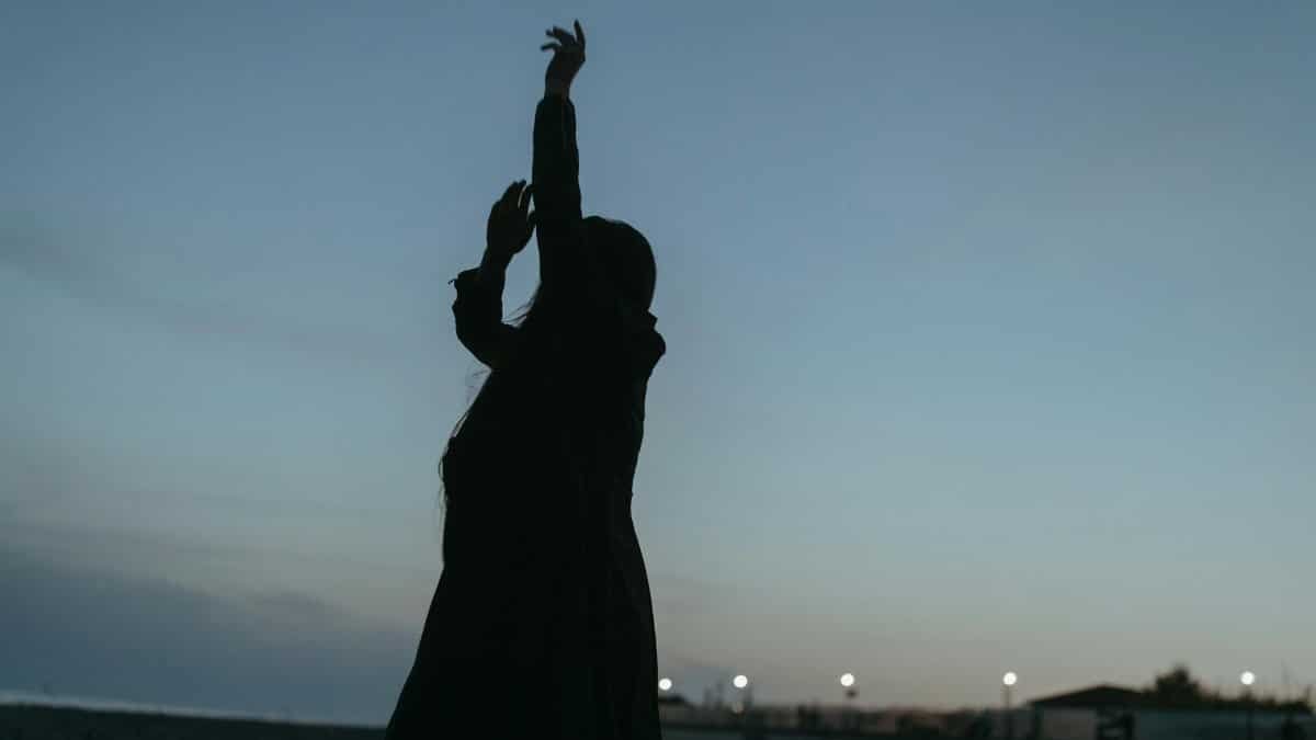 A silhouette of a woman with hands raised against a dusky sky, evoking tranquility and freedom.