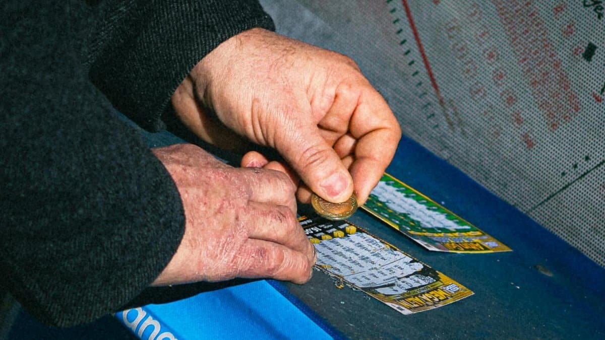 Hands using a coin to scratch off a lottery ticket on a blue table.