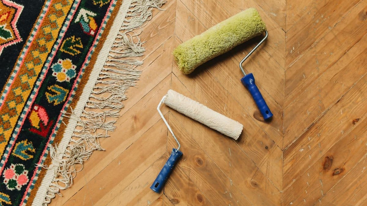 Two paint rollers on a wooden floor next to a colorful rug, symbolizing home renovation.
