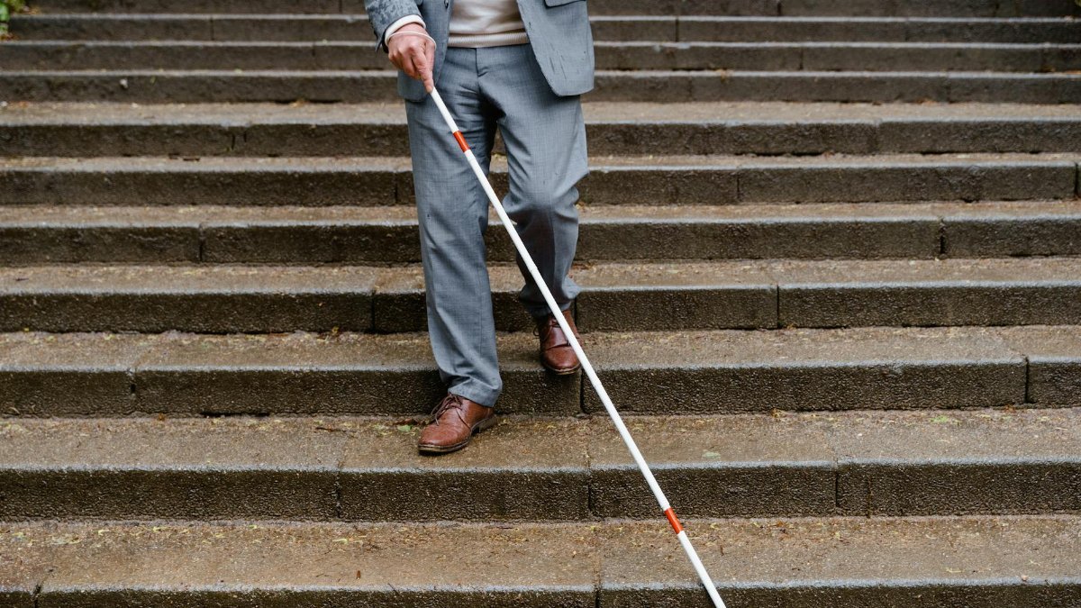Man with visual impairment using white cane to walk down outdoor steps.