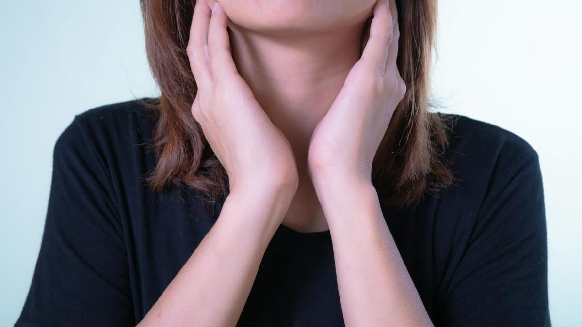Close-up of a woman touching her neck, possibly indicating discomfort or throat pain.