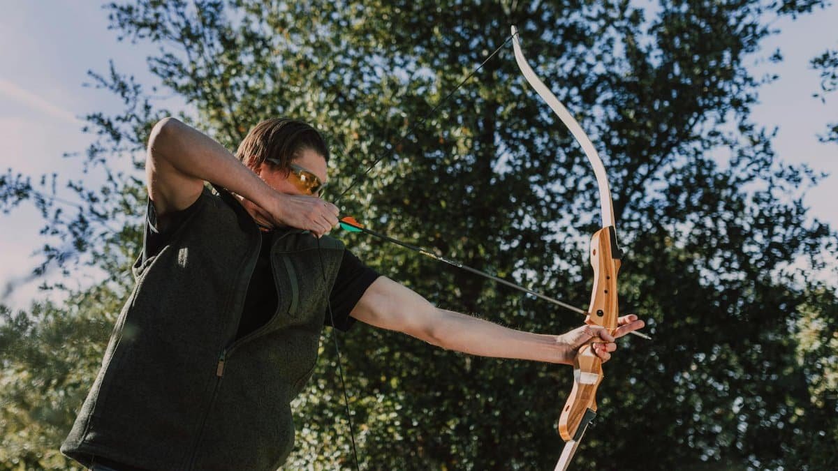 Man practicing archery with recurve bow outdoors on a sunny day.