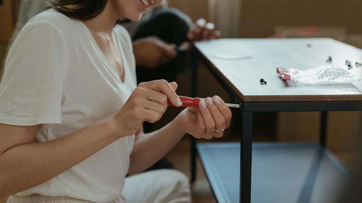 Woman smiling while assembling a table using a screwdriver in a home setting.