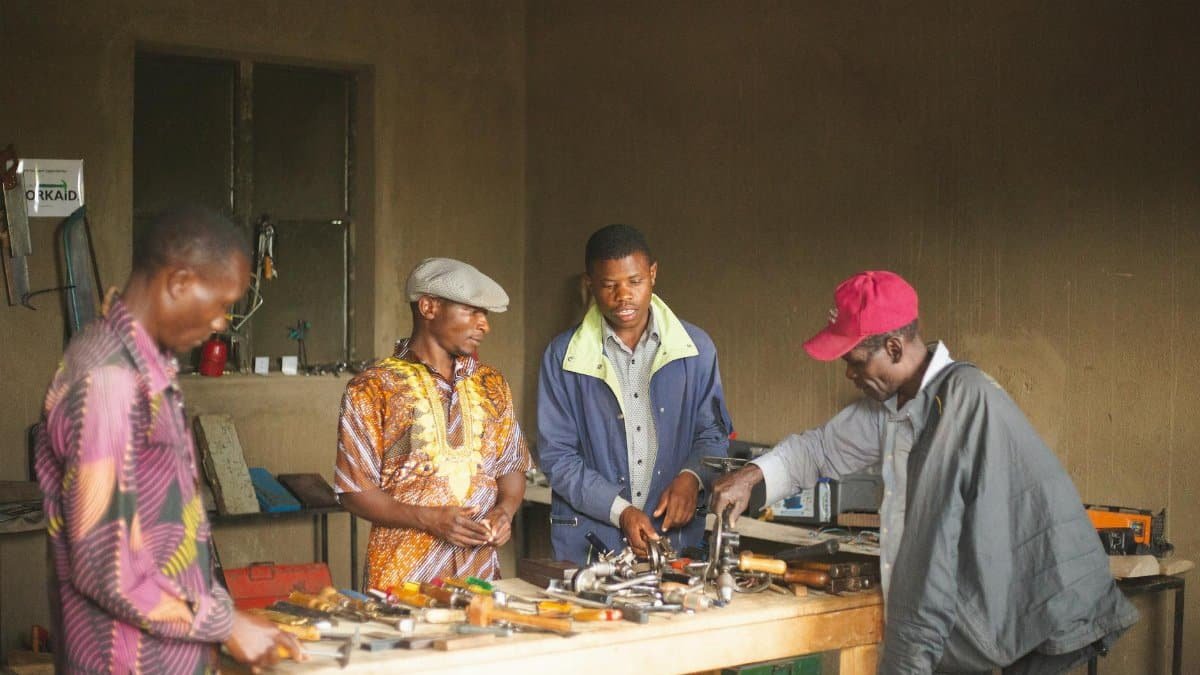 Group of men collaborating in a Ugandan workshop surrounded by tools and equipment.