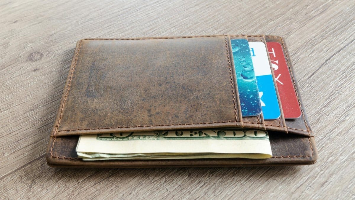 A brown leather wallet with cash and credit cards on a wooden surface.