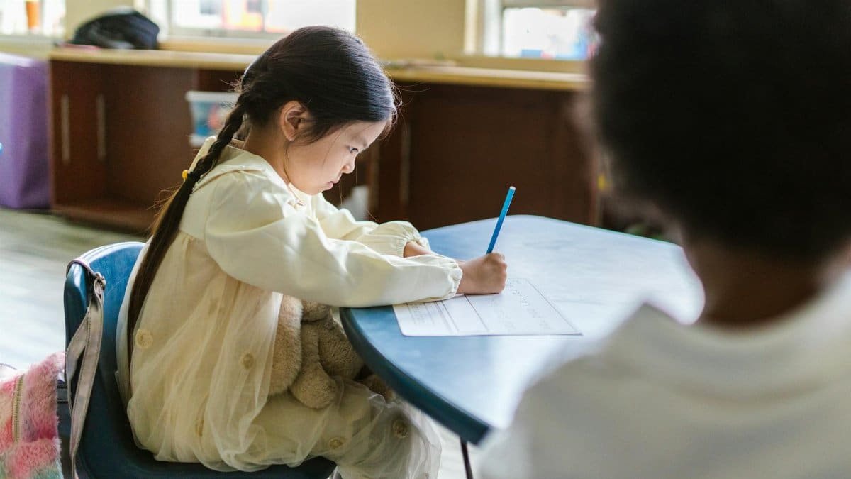 A young child intensely focused on writing at a classroom table, showing concentration and learning.