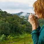 A woman enjoys morning coffee while gazing at a scenic mountain view.