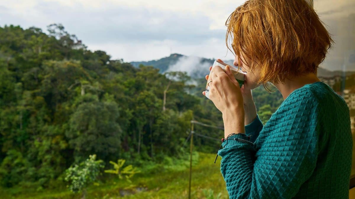 A woman enjoys morning coffee while gazing at a scenic mountain view.