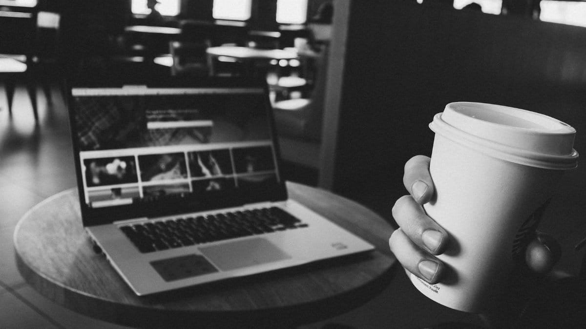 A cozy coffee shop scene with a laptop and coffee cup on a table, perfect for tech and lifestyle themes.