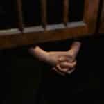 Hands clasped in prayer inside a wooden confessional, symbolizing faith and introspection.