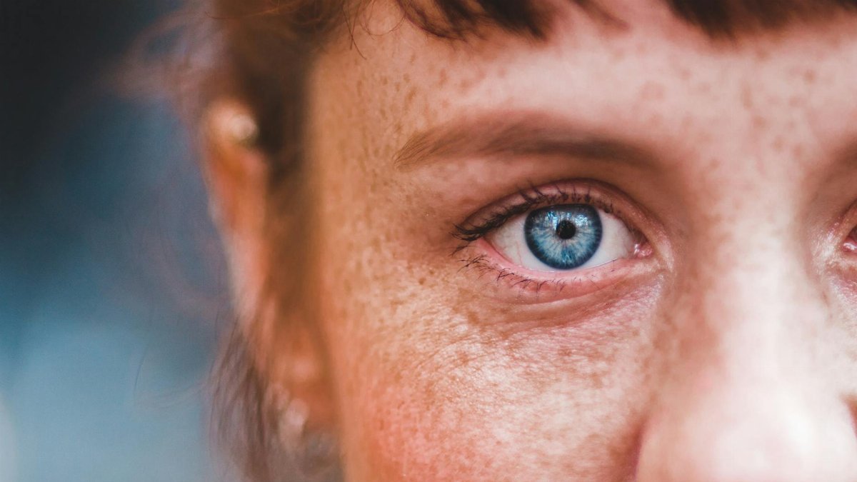 A detailed close-up of a woman's blue eye and freckles, showcasing natural beauty.