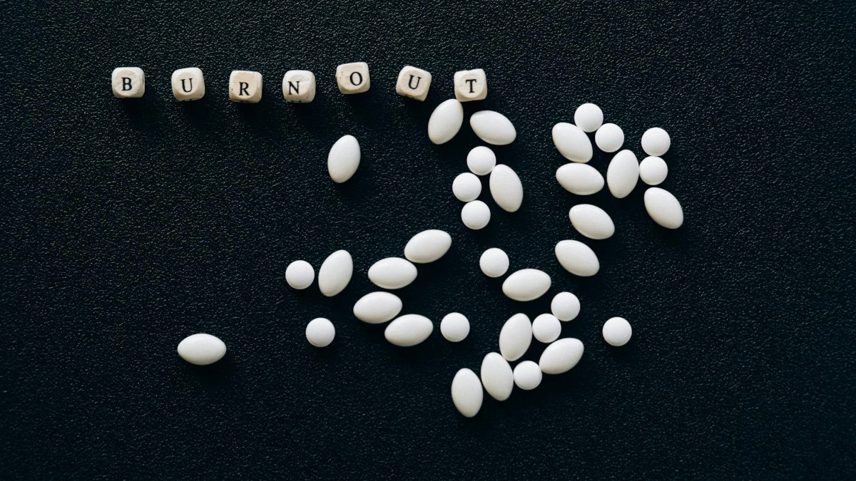 White pills arranged on a black surface spelling 'burnout', symbolizing stress and fatigue.