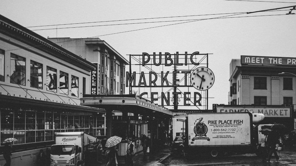 Black and white view of Seattle's Pike Place Market during rain, featuring iconic public market sign.
