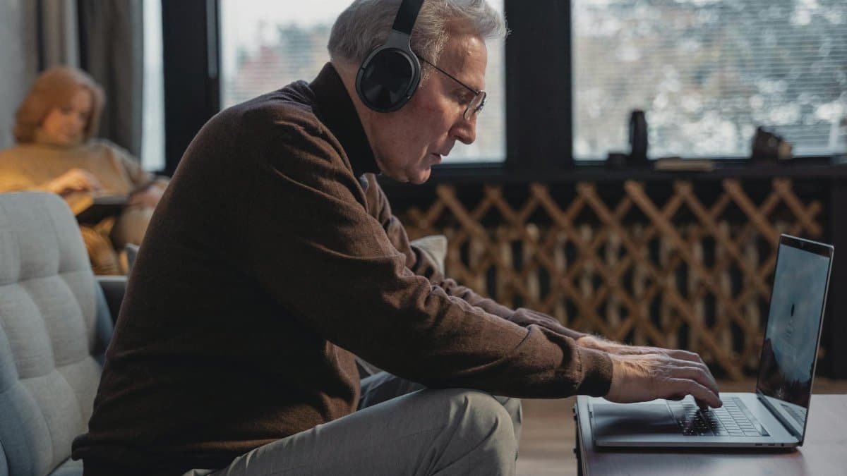 Senior man wearing headphones using laptop for a virtual meeting from home.