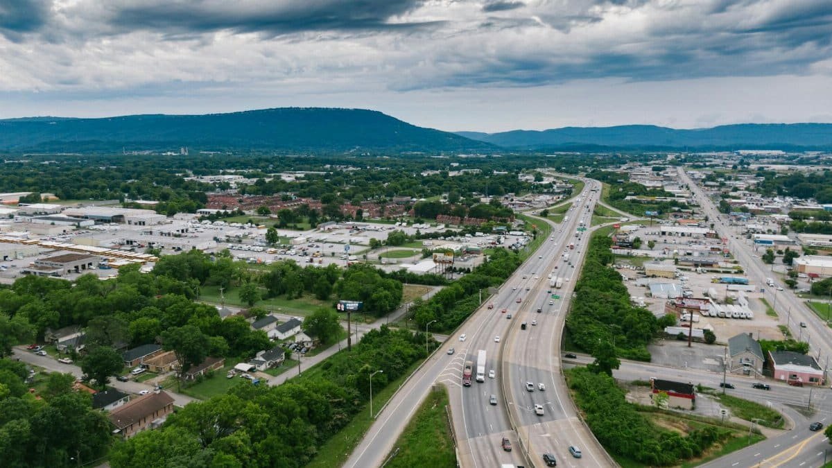 Aerial view of a busy highway in Chattanooga with lush greenery and urban landscape under cloudy skies.