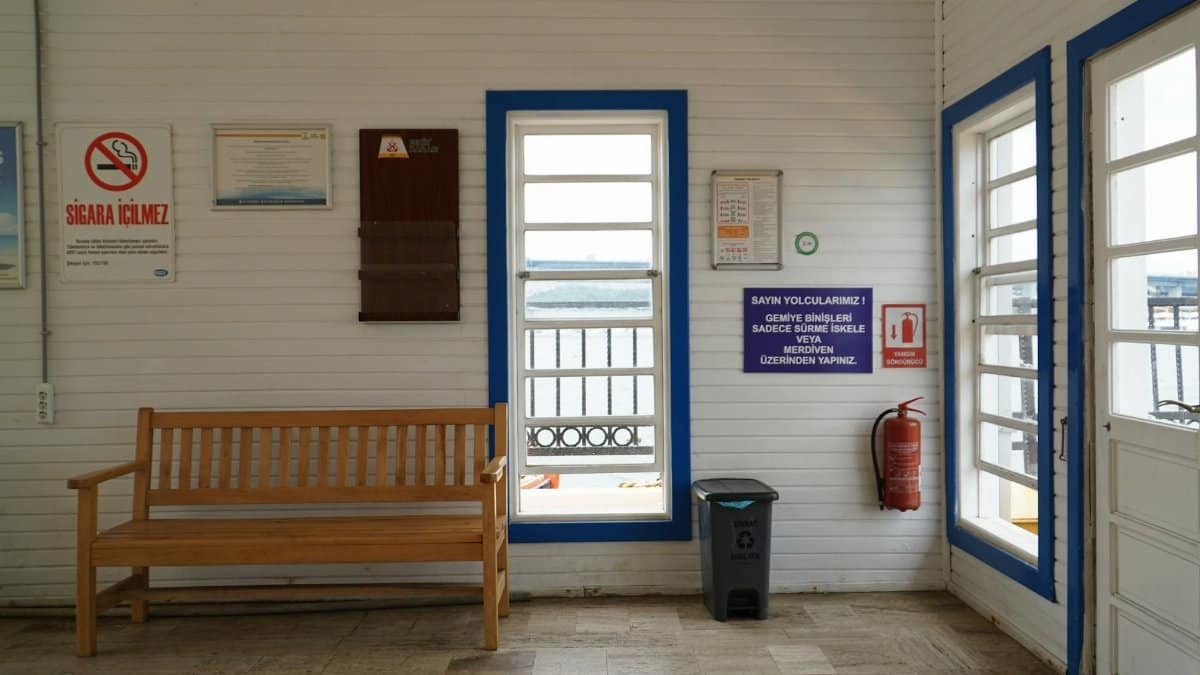 Cozy indoor waiting area in Istanbul with a wooden bench and various signs on white paneled walls.
