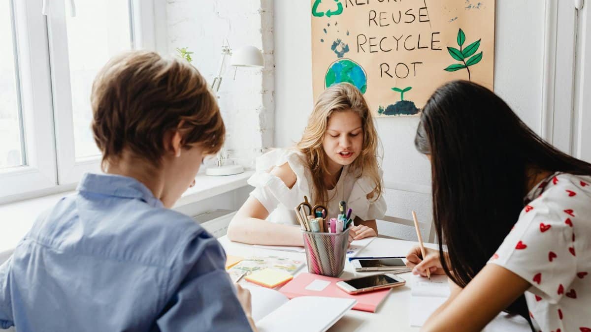 Three students working on a sustainable project with art supplies, promoting eco-awareness.