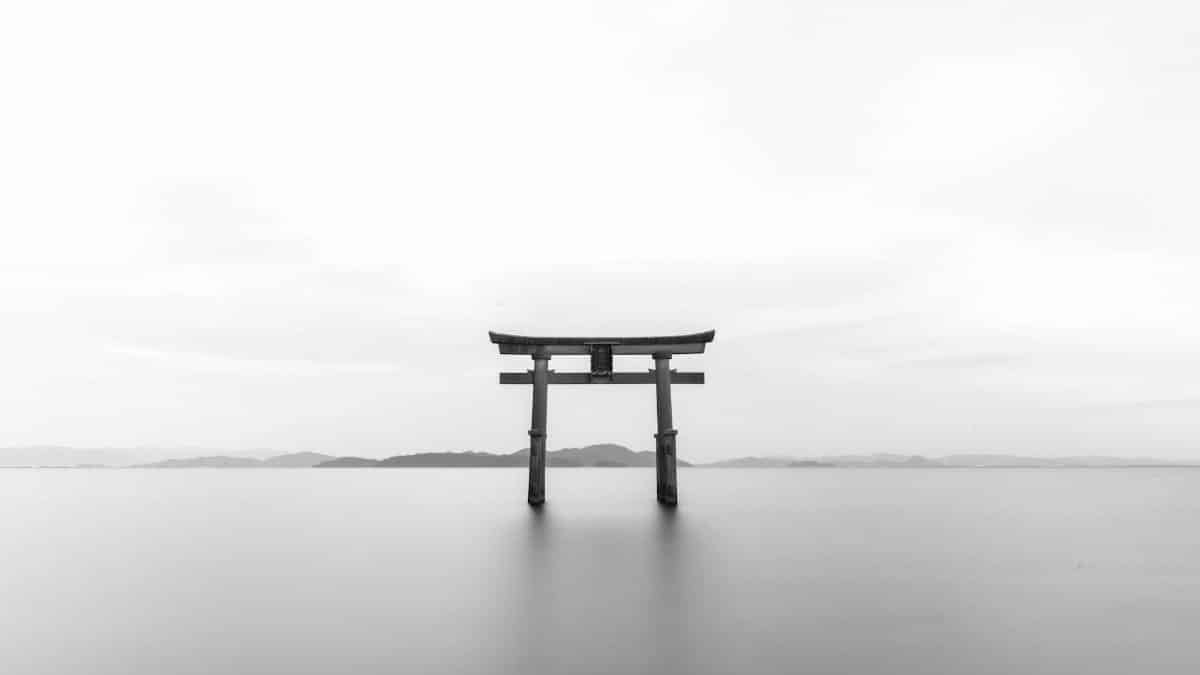 Serene black and white image of a torii gate standing in calm waters, symbolizing tranquility.