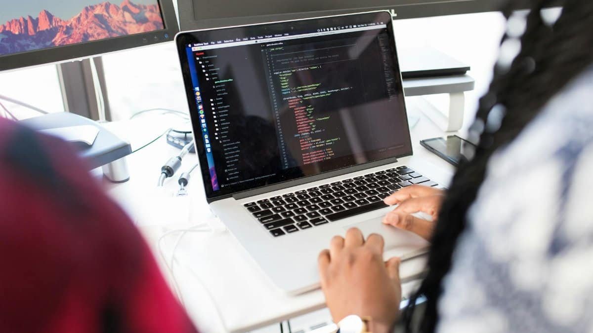 A woman coding on a laptop in a modern office environment with multiple monitors.