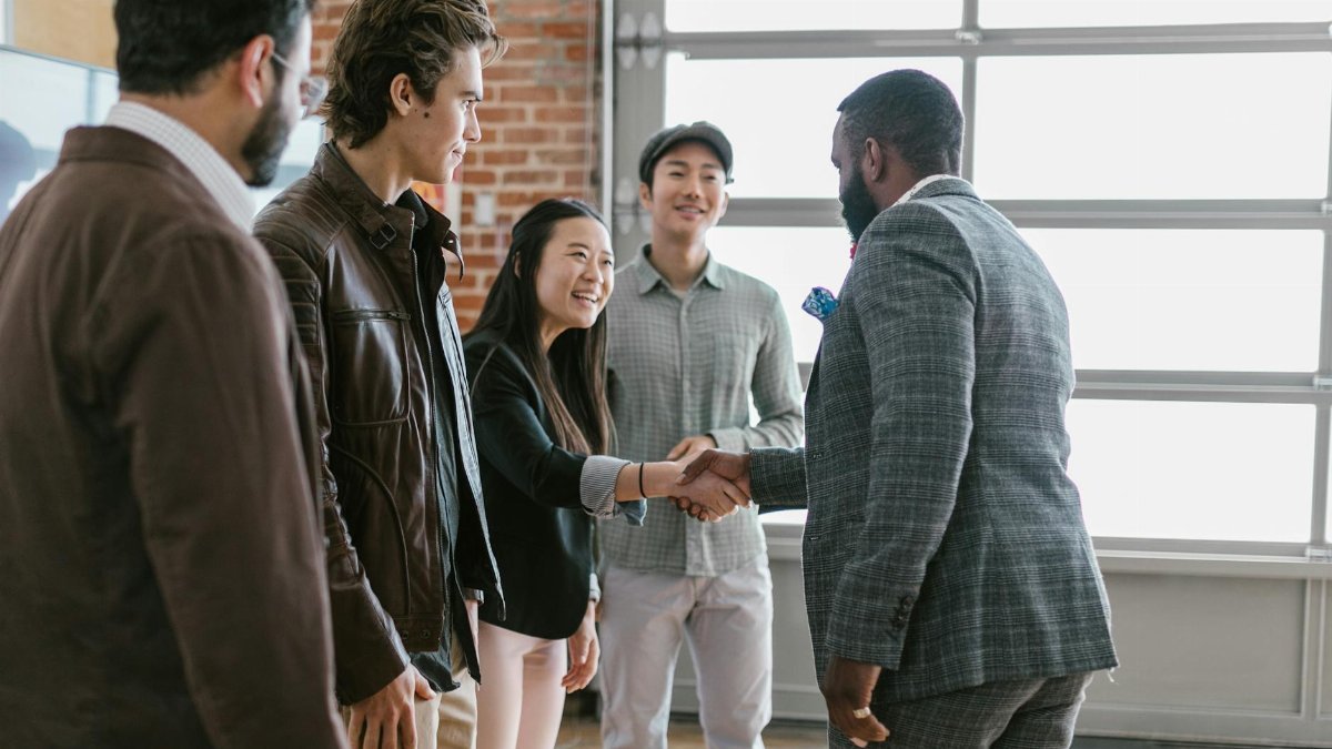 A diverse group of business professionals engaging in a handshake and discussion in a modern office space.