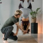 Aerial yoga class with an instructor aiding a student on a suspended hammock indoors.
