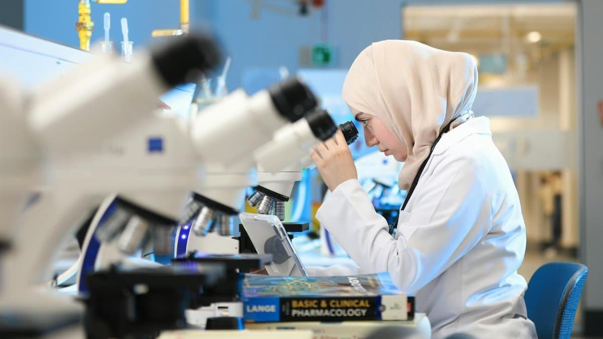 A scientist in a lab coat examines samples through a microscope in a modern laboratory setting.