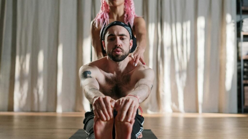 A yoga instructor assisting a student in a studio setting, focusing on health and wellbeing.