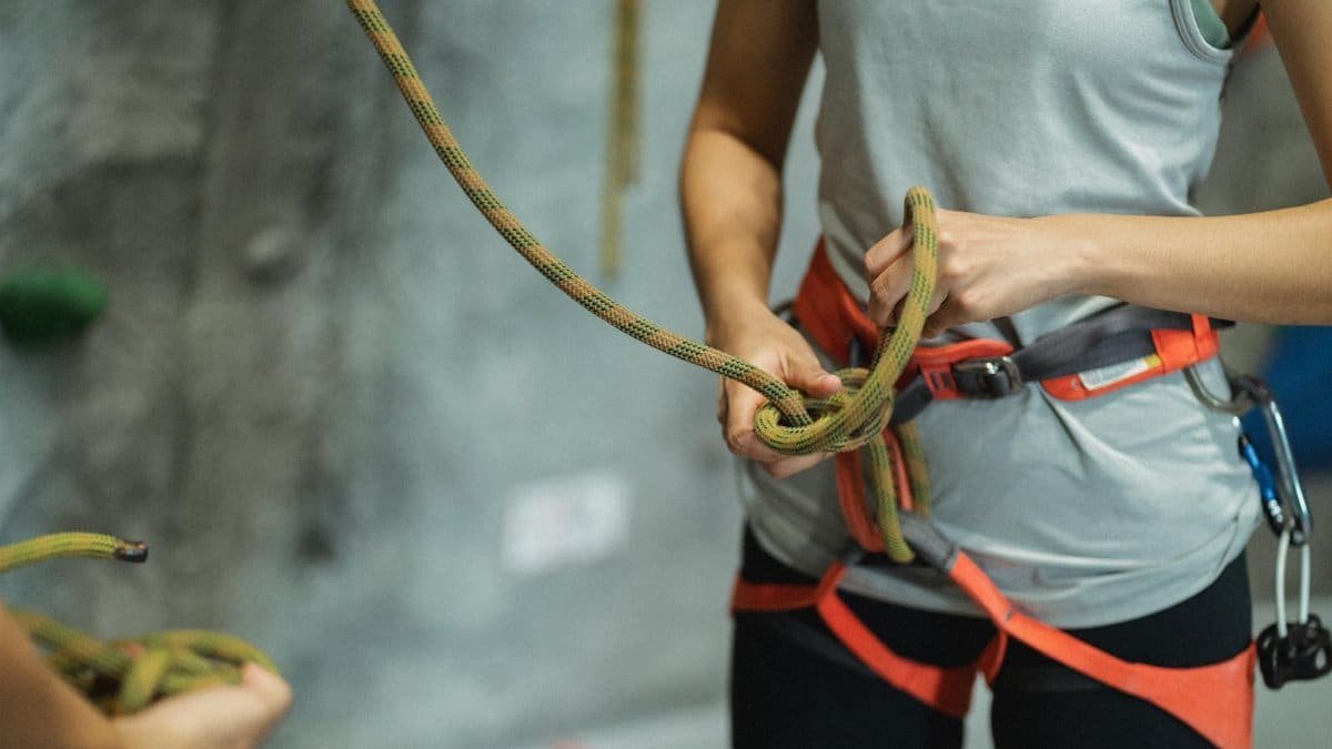 Woman preparing for indoor rock climbing, focusing on safety gear and rope management.