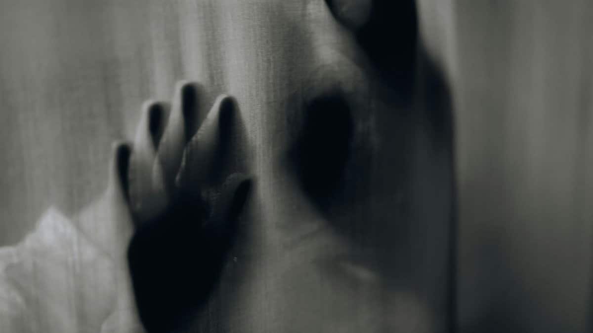 Blurred hands pressed against a curtain creating an eerie silhouette.