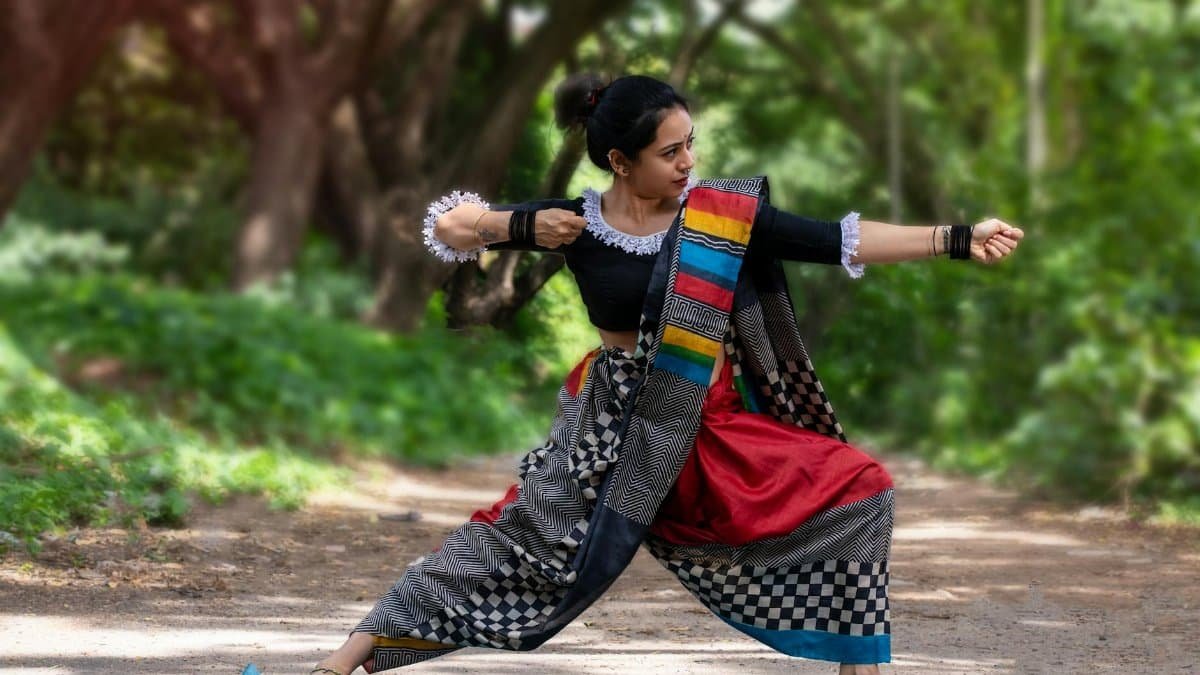 A woman performs yoga in a vibrant outfit on a forest path, embodying mindfulness and tradition.