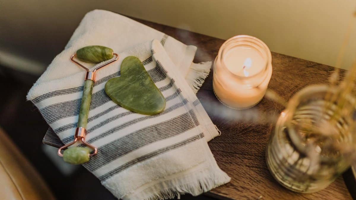 Calming spa setup featuring a jade roller, gua sha stone, and candle for relaxation and skincare.
