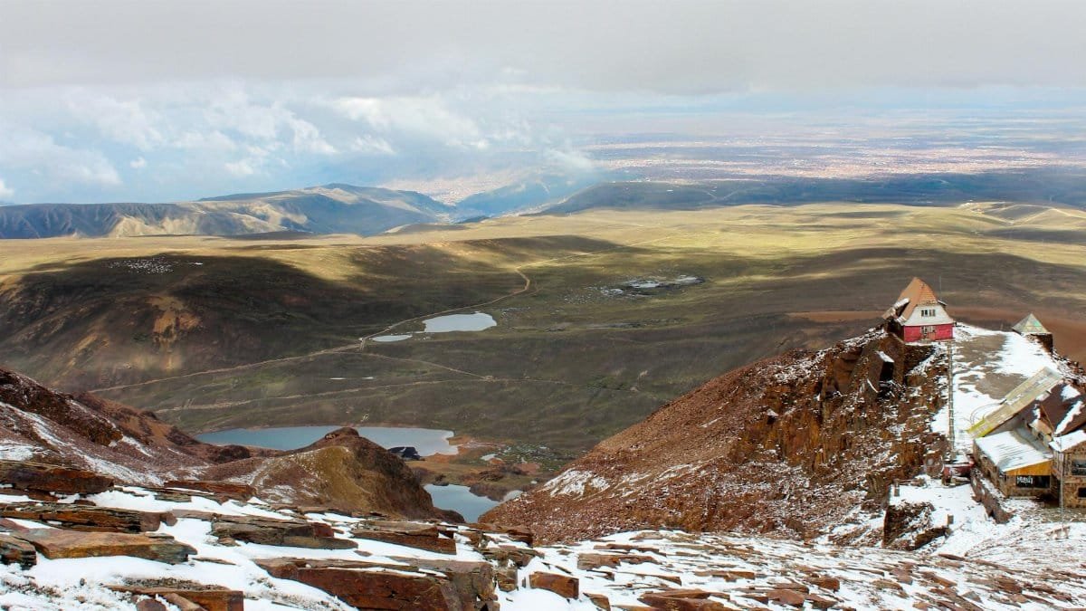 A stunning landscape of a snowy mountain with expansive valley views under a cloudy sky.