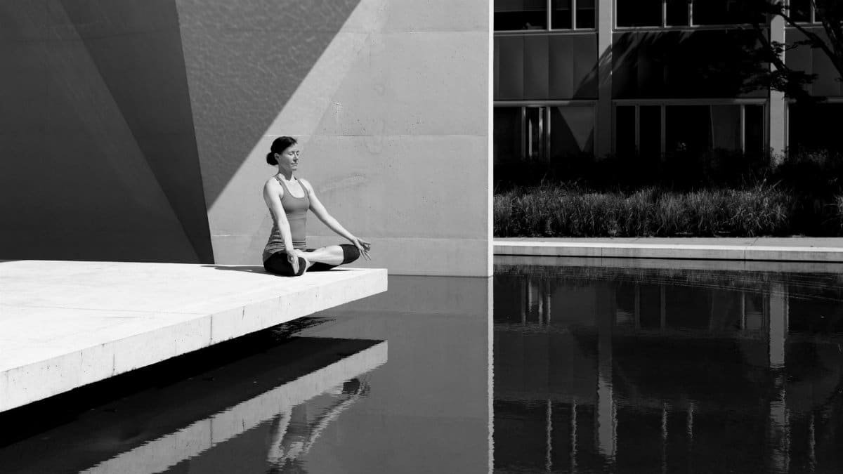 A woman meditating by a poolside, reflecting tranquility and focus in a minimalist setting.