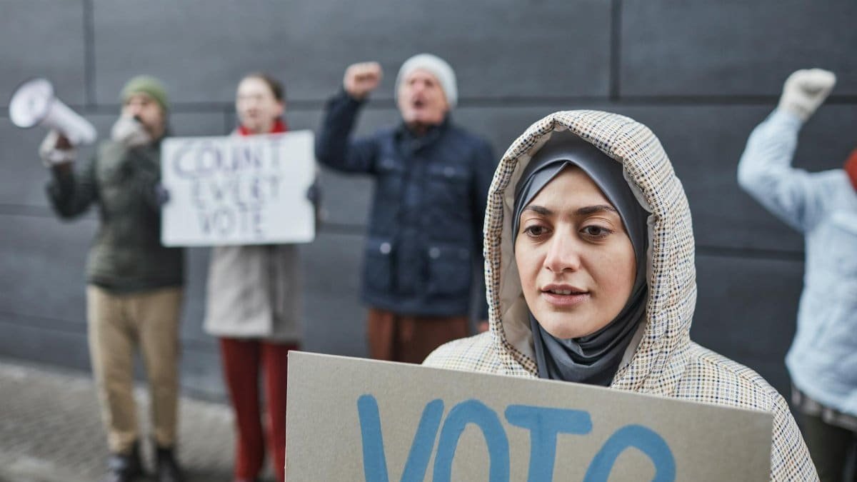 Close-up of a woman in a hijab holding a 'Vote' sign at a peaceful street protest advocating democracy.