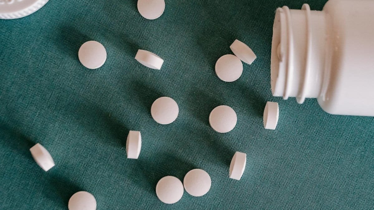 Top view of similar small round white pills spilled from plastic container on green surface