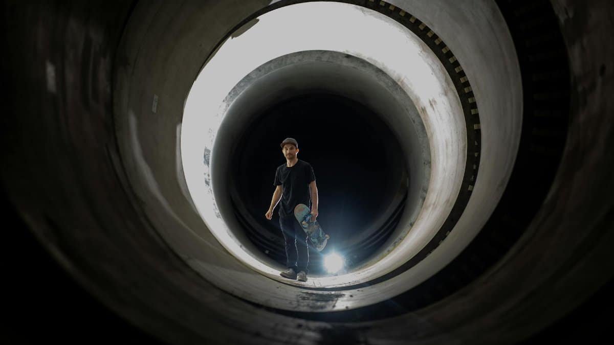 A skateboarder poses dramatically in a dark tunnel with a spotlight effect, creating a striking visual.