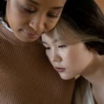 A tender moment of support between two women indoors, conveying care.