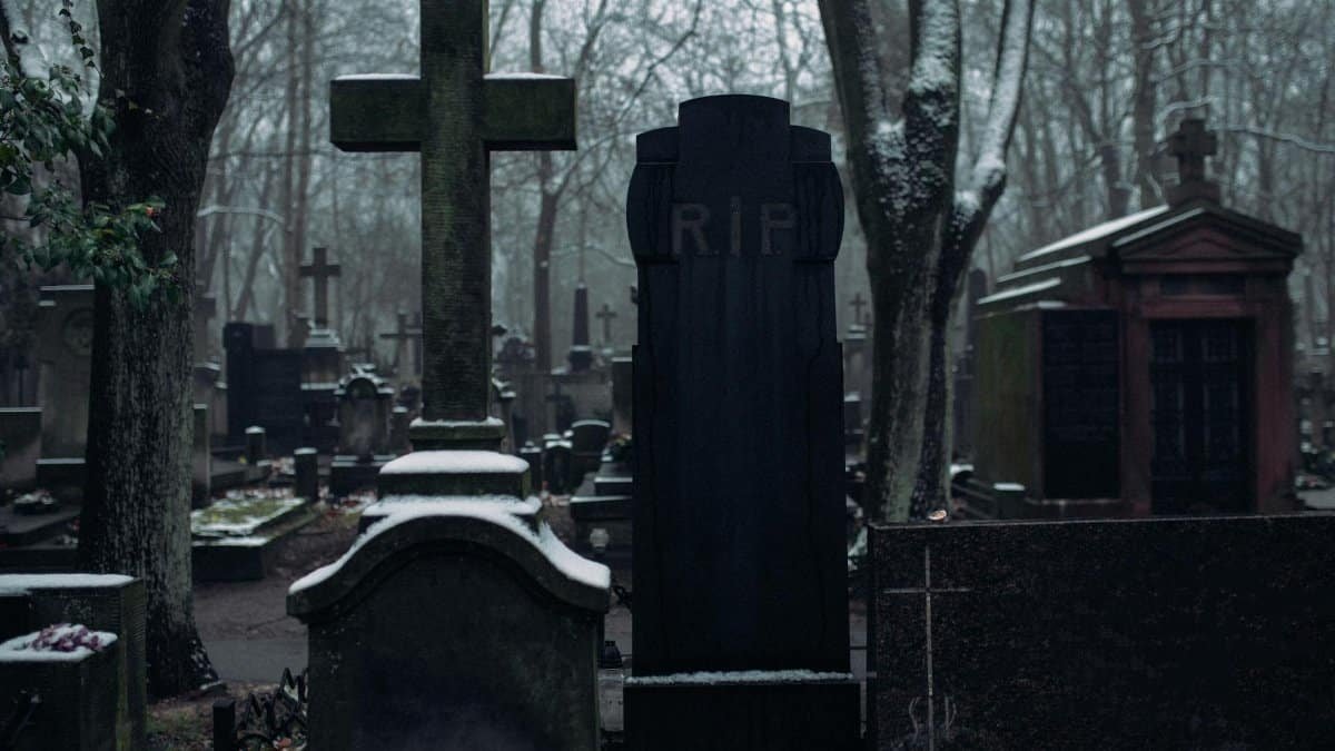 A tranquil cemetery with snow-covered gravestones amidst bare trees, creating a serene yet eerie atmosphere.