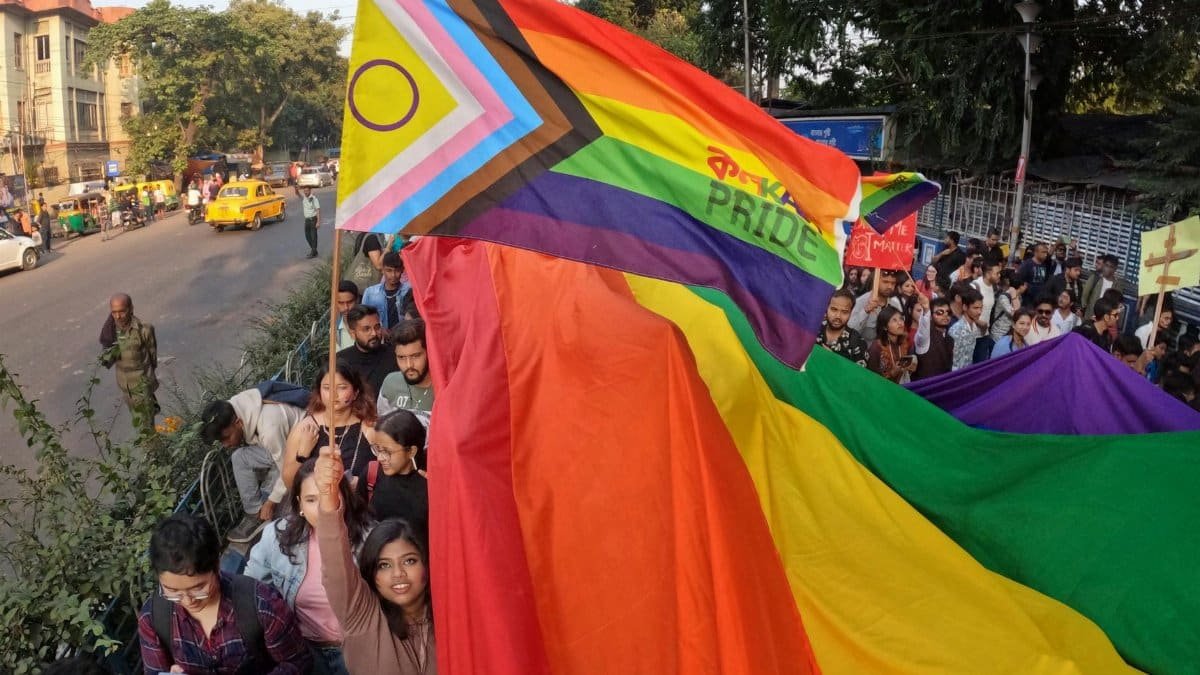 Vibrant LGBTQ+ pride parade in Kolkata, India with participants and colorful flags.