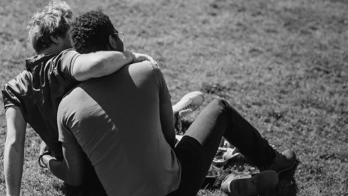 A loving couple sitting together on grass in a black and white outdoor portrait.