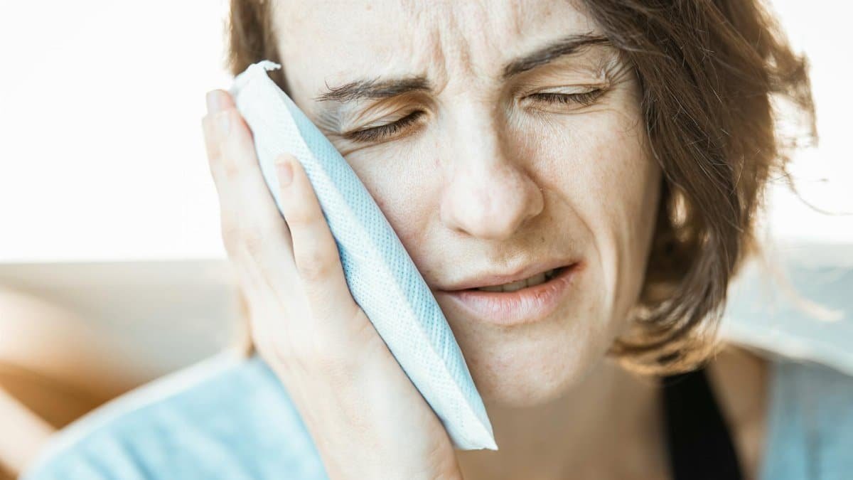A woman in discomfort applying a cold compress to her cheek for relief from toothache pain.