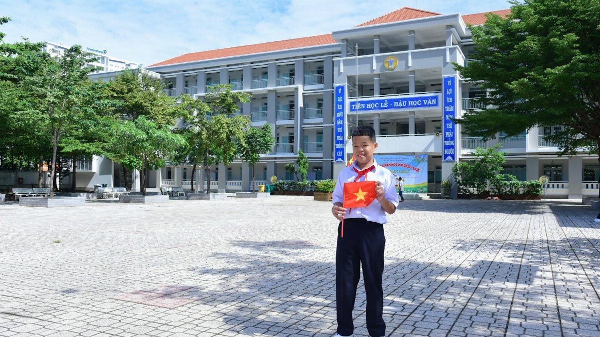 Young Vietnamese student holding national flag in bright schoolyard setting.