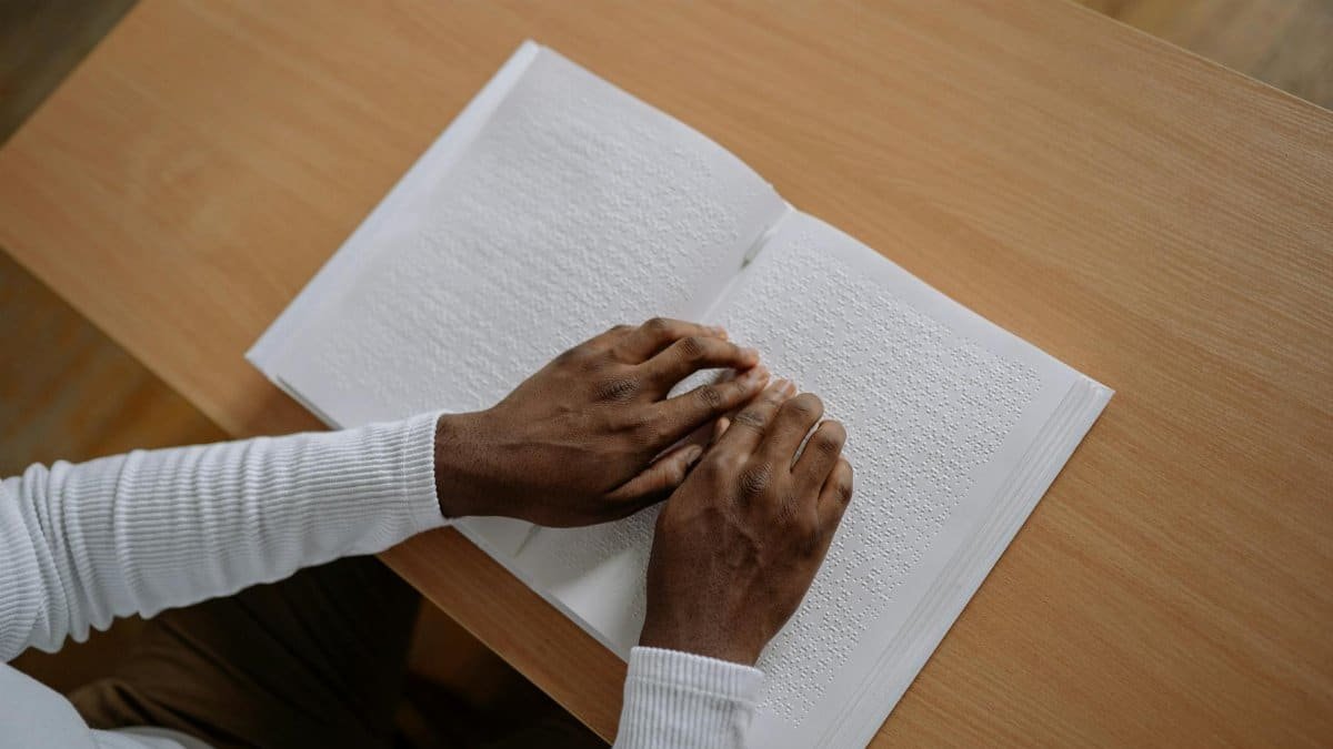 Close-up of hands reading braille in a book, symbolizing visual impairment awareness.