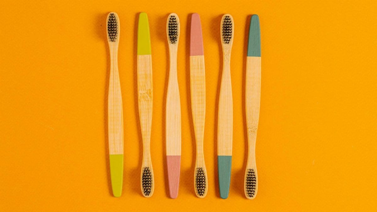 Six bamboo toothbrushes with colorful tips on a vibrant orange surface.