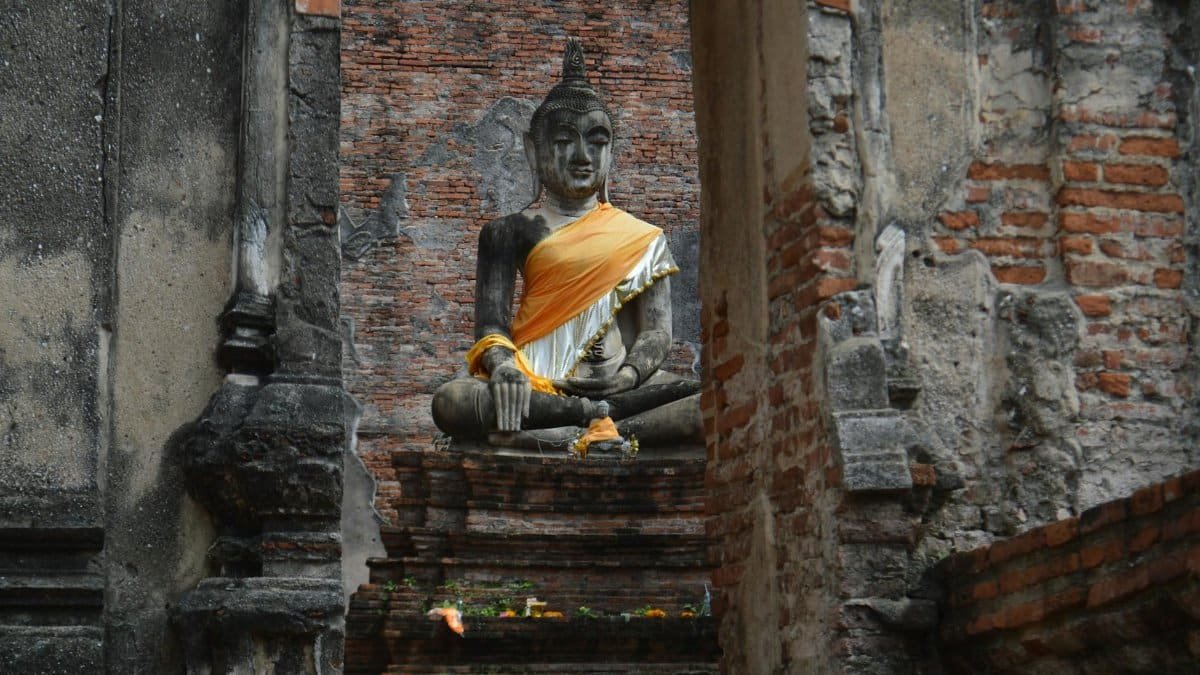 Majestic Buddha statue draped in orange robe amidst ancient temple ruins, conveying serenity and history.