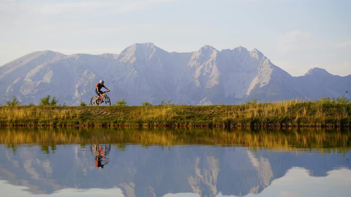 A mountain biker rides along a scenic lake with majestic mountain views in Tirol, Austria.