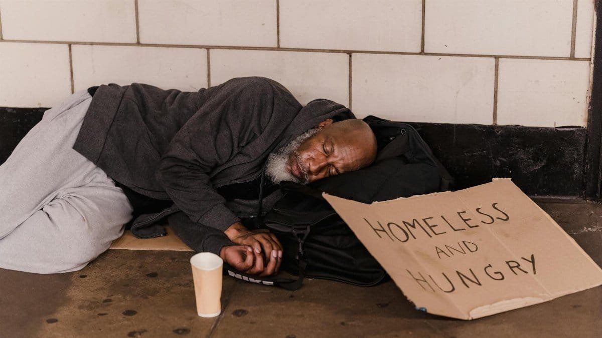 A homeless man sleeping on the street with a cardboard sign, capturing urban hardship.