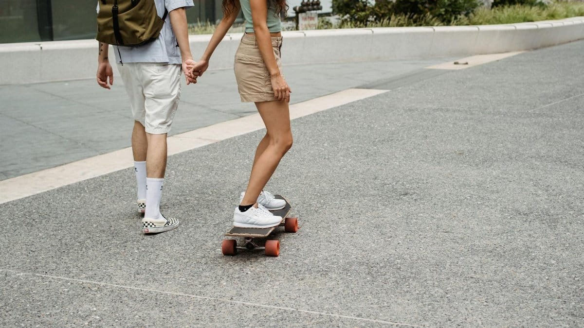 A couple enjoying a summer urban stroll while holding hands and skateboarding on a city street.