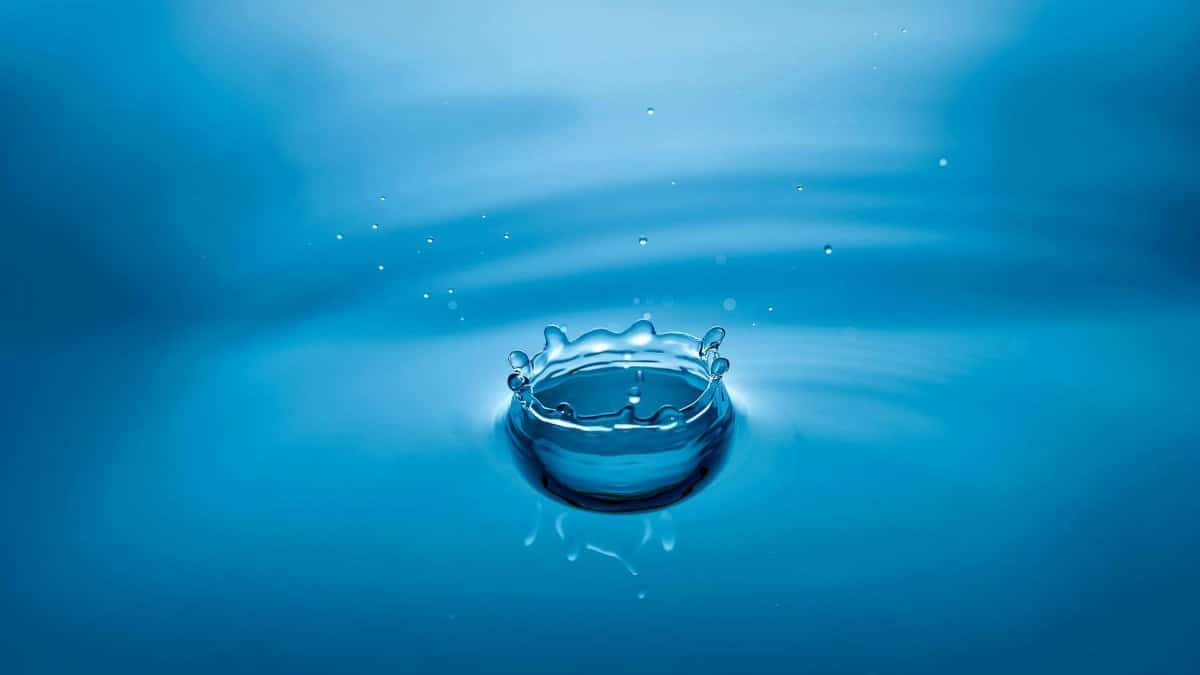 High-speed photo of a blue water droplet creating ripples and splash effects.