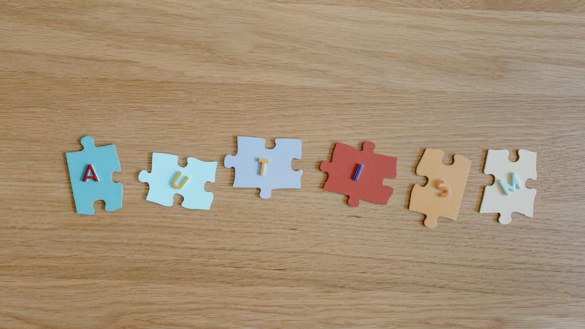 Colorful puzzle pieces spelling 'autism' on a wooden surface, promoting autism awareness.